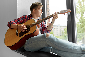 Image showing young man playing guitar sitting on windowsill