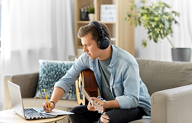 Image showing man in headphones with guitar, notes and laptop