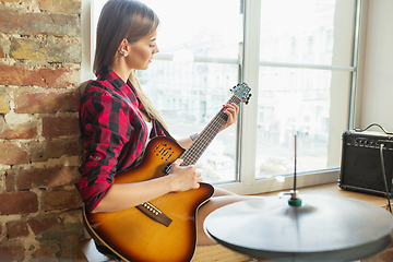 Image showing Woman recording music, singing and playing guitar while sitting in loft workplace or at home