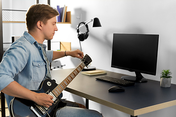 Image showing young man with computer playing guitar at home