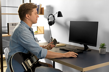 Image showing young man with computer and bass guitar at home