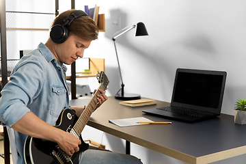 Image showing man in headphones playing bass guitar at home