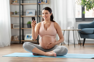 Image showing happy pregnant woman with phone doing yoga at home