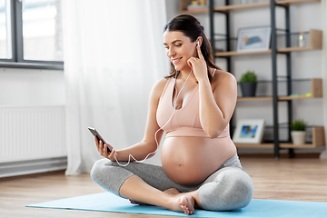 Image showing pregnant woman with earphones doing yoga at home