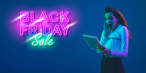 Image showing Portrait of young woman in neon light on blue backgound. The human emotions, black friday, cyber monday, purchases, sales, finance concept. Neoned lettering.