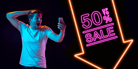 Image showing Portrait of young man in neon light on dark backgound. The human emotions, black friday, cyber monday, purchases, sales, finance concept. Neoned lettering.