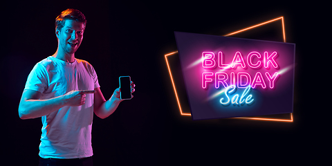 Image showing Portrait of young man in neon light on dark backgound. The human emotions, black friday, cyber monday, purchases, sales, finance concept. Neoned lettering.