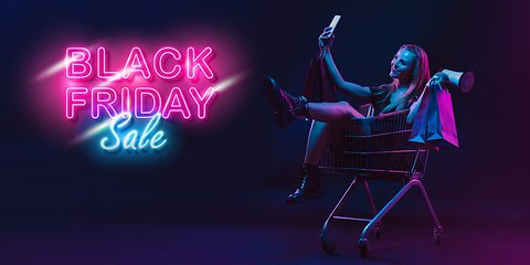 Image showing Portrait of young woman in neon light on dark backgound. The human emotions, black friday, cyber monday, purchases, sales, finance concept. Neoned lettering.