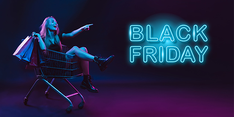 Image showing Portrait of young woman in neon light on dark backgound. The human emotions, black friday, cyber monday, purchases, sales, finance concept. Neoned lettering.