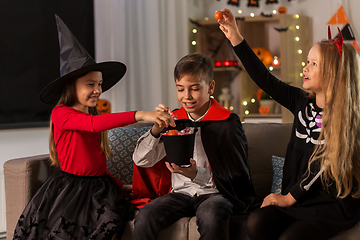 Image showing kids in halloween costumes sharing candies at home