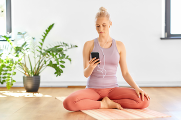 Image showing woman with phone and earphones doing yoga at home