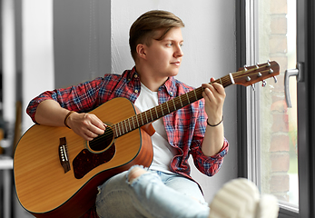 Image showing young man playing guitar sitting on windowsill