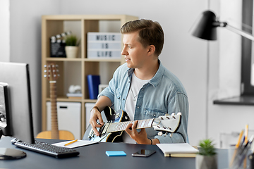 Image showing young man with computer playing guitar at home