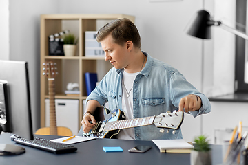 Image showing young man with computer playing guitar at home