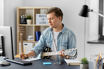 Image showing man with guitar writing to music book at home