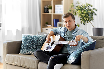 Image showing young man playing guitar sitting on sofa at home