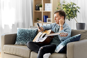 Image showing man with guitar, earphones and smartphone at home