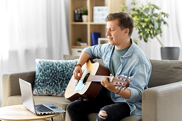 Image showing young man with laptop playing guitar at home