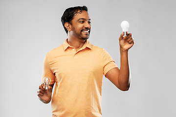 Image showing smiling indian man comparing different light bulbs