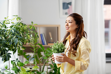 Image showing happy asian woman with flower in pot at home