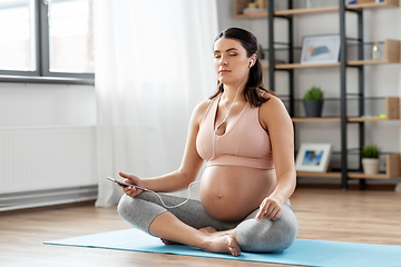 Image showing pregnant woman with earphones doing yoga at home