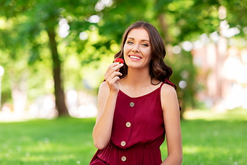 Image showing happy woman eating strawberry at summer park