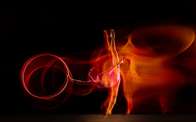 Image showing Young flexible female gymnast isolated on black studio background in mixed light,