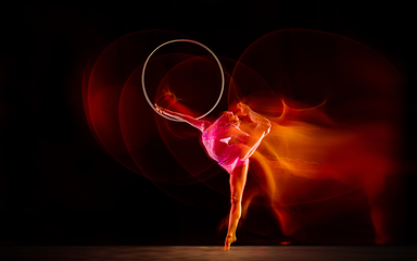 Image showing Young flexible female gymnast isolated on black studio background in mixed light,