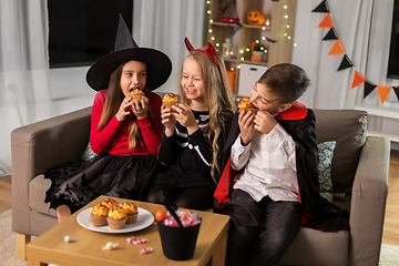 Image showing kids in halloween costumes eating cupcakes at home
