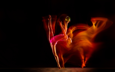 Image showing Young flexible female gymnast isolated on black studio background in mixed light,