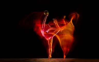 Image showing Young flexible female gymnast isolated on black studio background in mixed light,