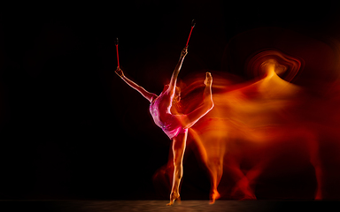 Image showing Young flexible female gymnast isolated on black studio background in mixed light,