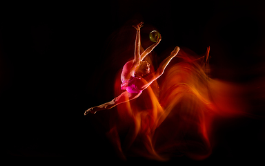 Image showing Young flexible female gymnast isolated on black studio background in mixed light,