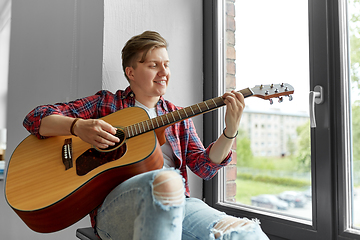 Image showing young man playing guitar sitting on windowsill