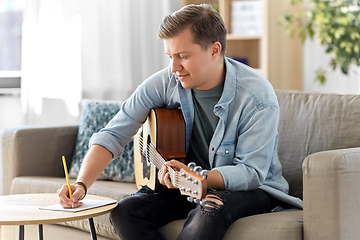 Image showing man with guitar writing to music book at home