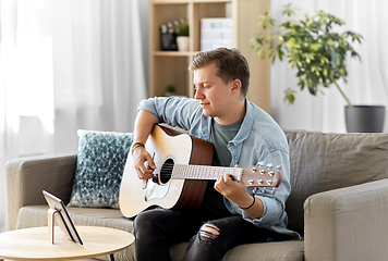 Image showing young man with tablet pc playing guitar at home