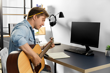 Image showing young man with music book playing guitar at home