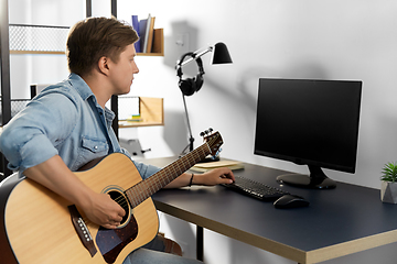 Image showing young man with computer playing guitar at home