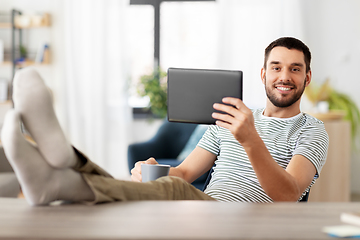 Image showing man with tablet pc resting feet on table at home