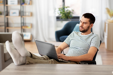 Image showing man with laptop resting feet on table at home