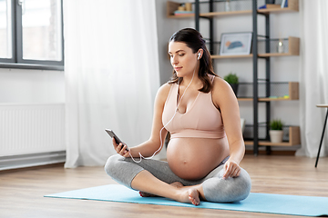 Image showing pregnant woman with earphones doing yoga at home