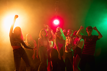 Image showing A crowd of people in silhouette raises their hands on dancefloor on neon light background