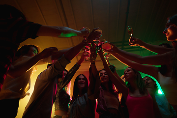 Image showing A crowd of people in silhouette raises their hands on dancefloor on neon light background