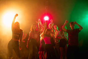 Image showing A crowd of people in silhouette raises their hands on dancefloor on neon light background