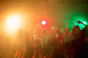 Image showing A crowd of people in silhouette raises their hands on dancefloor on neon light background