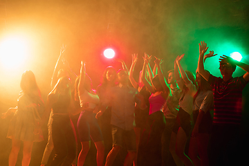 Image showing A crowd of people in silhouette raises their hands on dancefloor on neon light background