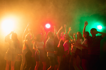 Image showing A crowd of people in silhouette raises their hands on dancefloor on neon light background