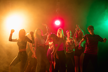 Image showing A crowd of people in silhouette raises their hands on dancefloor on neon light background