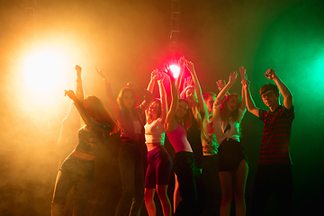 Image showing A crowd of people in silhouette raises their hands on dancefloor on neon light background