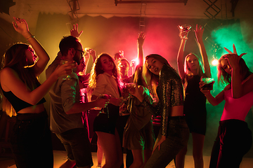 Image showing A crowd of people in silhouette raises their hands on dancefloor on neon light background